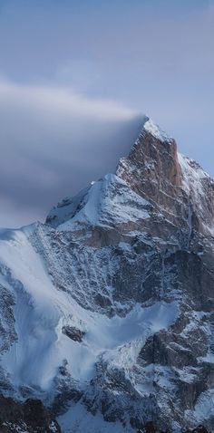 a very tall mountain covered in snow under a cloudy sky