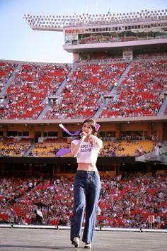 a woman holding a purple scarf in front of a stadium full of people with red seats