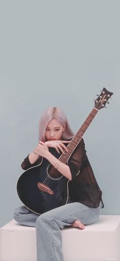 a woman sitting on top of a white box holding an acoustic guitar in her hands