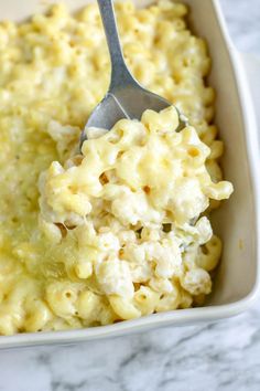 a spoon with macaroni and cheese is in a white casserole dish