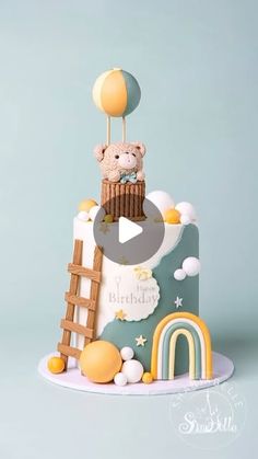 a birthday cake with a teddy bear on top and rainbows in the sky above it