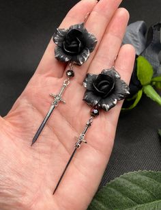 These Gothic sword earrings are a bold, handcrafted accessory featuring black polymer clay roses and Czech glass beads. The silver-tone sword dangles beneath the meticulously crafted flower, adding an edgy touch to your alternative style. Perfect for Gothic, punk, or dark fashion lovers, these earrings stand out for their detailed craftsmanship. Whether you have pierced ears or prefer clip-ons, the earrings come with both options to ensure they suit everyone's style. The combination of the dark Handmade Black Fantasy Earrings, Nickel-free Black Polymer Clay Jewelry, Gothic Polymer Clay, Gothic Piercings, Gothic Jewelry Diy, Clay Roses, Dark Earrings, Earrings Stand, Dagger Earrings