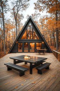 a - frame cabin in the woods with picnic table and benches on wooden decking