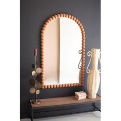 a mirror sitting on top of a wooden shelf next to a vase and candle holder