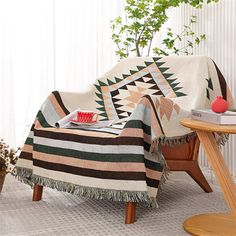 a blanket sitting on top of a wooden chair next to a table with a potted plant