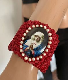 a woman's hand wearing a red bracelet with an image of jesus on it