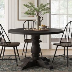 a dining room table with four chairs and a vase on top of it, in front of a window