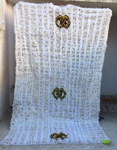 a white blanket with gold and green beads hanging from it's sides in front of a wall