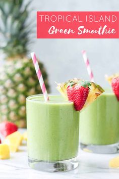 two glasses filled with green smoothie next to pineapple slices and strawberries on the side