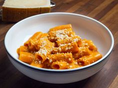 a white bowl filled with pasta and cheese on top of a wooden table next to bread