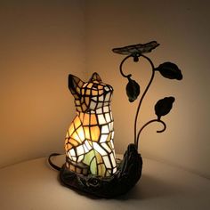 a cat lamp sitting on top of a table next to a flower vase with leaves