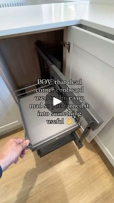 someone is opening the bottom drawer of a kitchen cabinet and pointing to it with their thumb