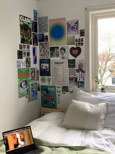 a laptop computer sitting on top of a bed next to pillows and pictures hanging on the wall