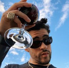 a man holding a wine glass up to his face with the sky in the background