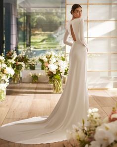 a woman in a white wedding dress standing on a wooden floor with flowers and greenery