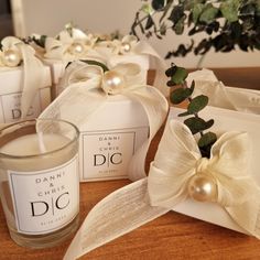 candles with bows and pearls on them sitting on a table next to some boxes that have flowers in them