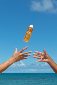 two hands reaching out towards each other to catch an orange liquid bottle in the air