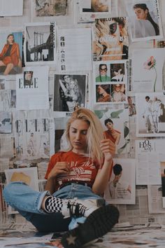 a woman sitting on the floor in front of a wall covered with pictures and posters