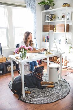 a woman sitting at a desk with a dog laying on the floor in front of her