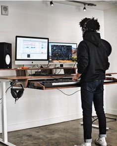 a person in a black hoodie standing at a desk with two computer monitors and keyboards