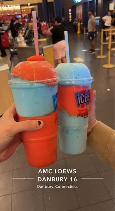 two orange and blue drinks are held up in front of each other with the words amc loews danbury 16