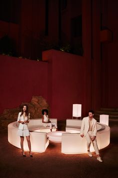 two people sitting on white couches in front of a red wall and some stairs