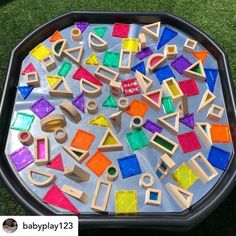 a black tray filled with lots of different colored wooden blocks and shapes on top of green grass