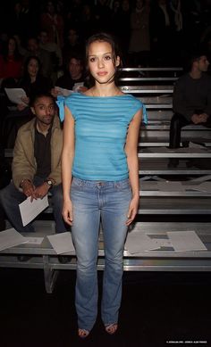 a woman standing in front of a group of people at a fashion show wearing jeans and sandals