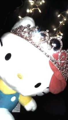 a hello kitty stuffed animal with a crown on it's head and lights in the background