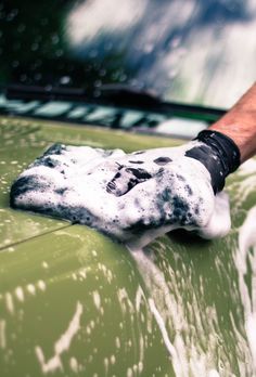 a man washing the hood of a green car with a black and white glove on it