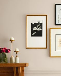 three framed pictures hang on the wall above a table with vases and flowers in front of it