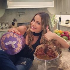 a woman is sitting on the kitchen counter holding two plates with food in them and giving thumbs up