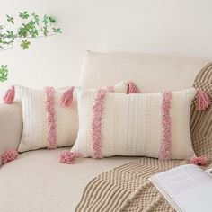 three pillows with tassels on them sitting on a couch next to a book