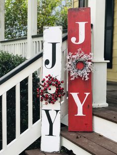 a red and white joy sign sitting on top of a porch next to a wreath