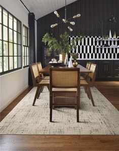 a dining room with black walls and wood flooring has a rug on the floor