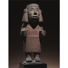 an ancient statue is displayed on a black surface with dark lighting in the back ground