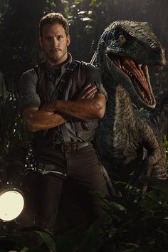 a man standing next to a dinosaur in the jungle with his arms crossed and eyes closed