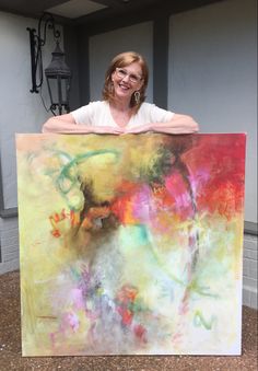 a woman holding up a large painting in front of her face and smiling at the camera