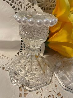 a glass vase sitting on top of a doily next to a yellow tulip