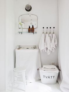 a white bathroom with towels hanging on the wall and two stools in front of it