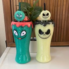 two decorated vases sitting on top of a white counter next to a potted plant