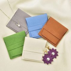 four different colored envelopes on a white sheet with a flower brooch and necklace