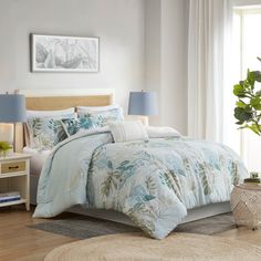 a bed with blue and white comforters in a bedroom next to a plant on the floor