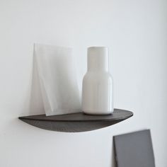 a white vase sitting on top of a shelf next to a paper towel dispenser