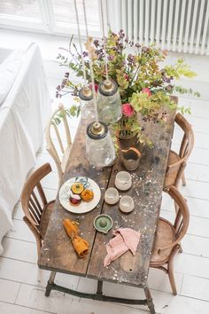 a wooden table topped with plates and vases filled with flowers next to a window