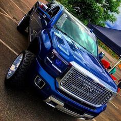 a large blue truck parked in a parking lot next to other cars and tents on the side of the road