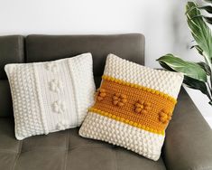 two crocheted pillows sitting on top of a couch next to a potted plant