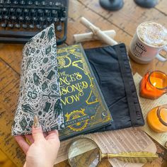 a person holding a book on top of a table next to glasses and other items