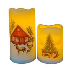 two lit candles sitting next to each other in front of a christmas tree and house