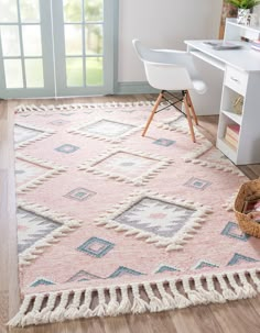 a pink rug with tassels on the floor in front of a desk and chair